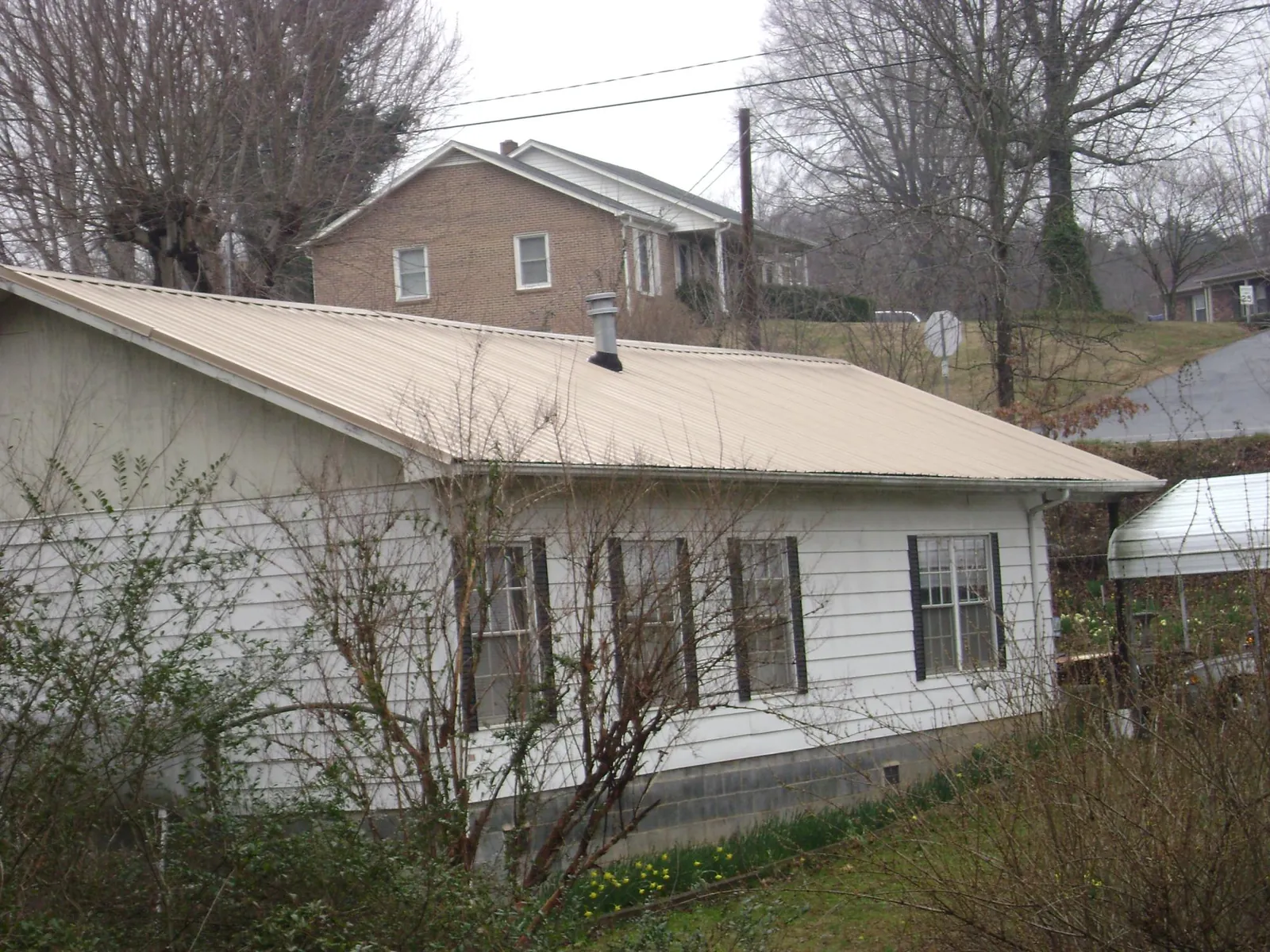 Tan metal roof on a white sided house set into a hillside — Commercial Roofing by Roofing Brothers in Denver